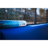 A close-up of a white and blue Yostoc sports equipment bat resting on a blue surface in front of a blurred net.