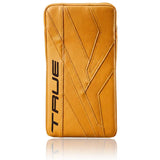 A tan hockey goalie blocker cover with diagonal stitched paneling and the brand name 'TRUE' printed vertically in black on the left side, shown on a white background with a reflection below.