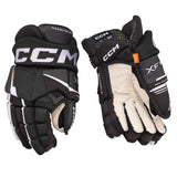 A pair of CCM X-Factor hockey gloves shown from both the backhand and palm sides, featuring a black and white color scheme with a small orange accent tab.