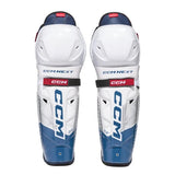 A pair of CCM Next Level hockey shin guards in white, blue, and navy, shown from the front against a white background.