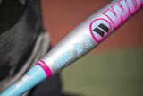 A close-up shot of a Worth Legit slo-pitch bat showing its silver barrel with pink and light blue accents, set against a blurred background.