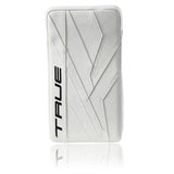 A white hockey goalie pad with diagonal stitched paneling and the brand name 'TRUE' printed vertically in black on the left side, shown against a white background with a soft reflection below.