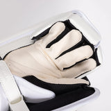 A close-up of a white and black hockey goalie glove resting inside white shin guards, showing the padded cream-colored finger sections and black mesh lining.