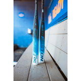 Two Easton baseball bats standing upright on a wooden bench in a dugout, with a blue wall and wood-paneled wall in the background.