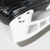 Close-up of a black carbon-fiber-look ice skate blade and white TUK metal mount on a light gray background.