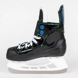 A black high-top ice skate boot with white laces, green stitching accents, and blue details, resting on a white plastic skate base against a light gray background.