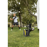 Child playing baseball with a pitching machine on a grassy field