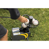 Person loading baseballs into a pitching machine on grass
